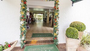 La entrada del Hotel Green Village con un arco decorativo navideño, un felpudo y un suelo de baldosas.