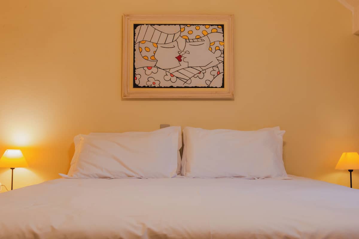 A bed with white linens, two bedside lamps, and a framed abstract artwork on the wall.
