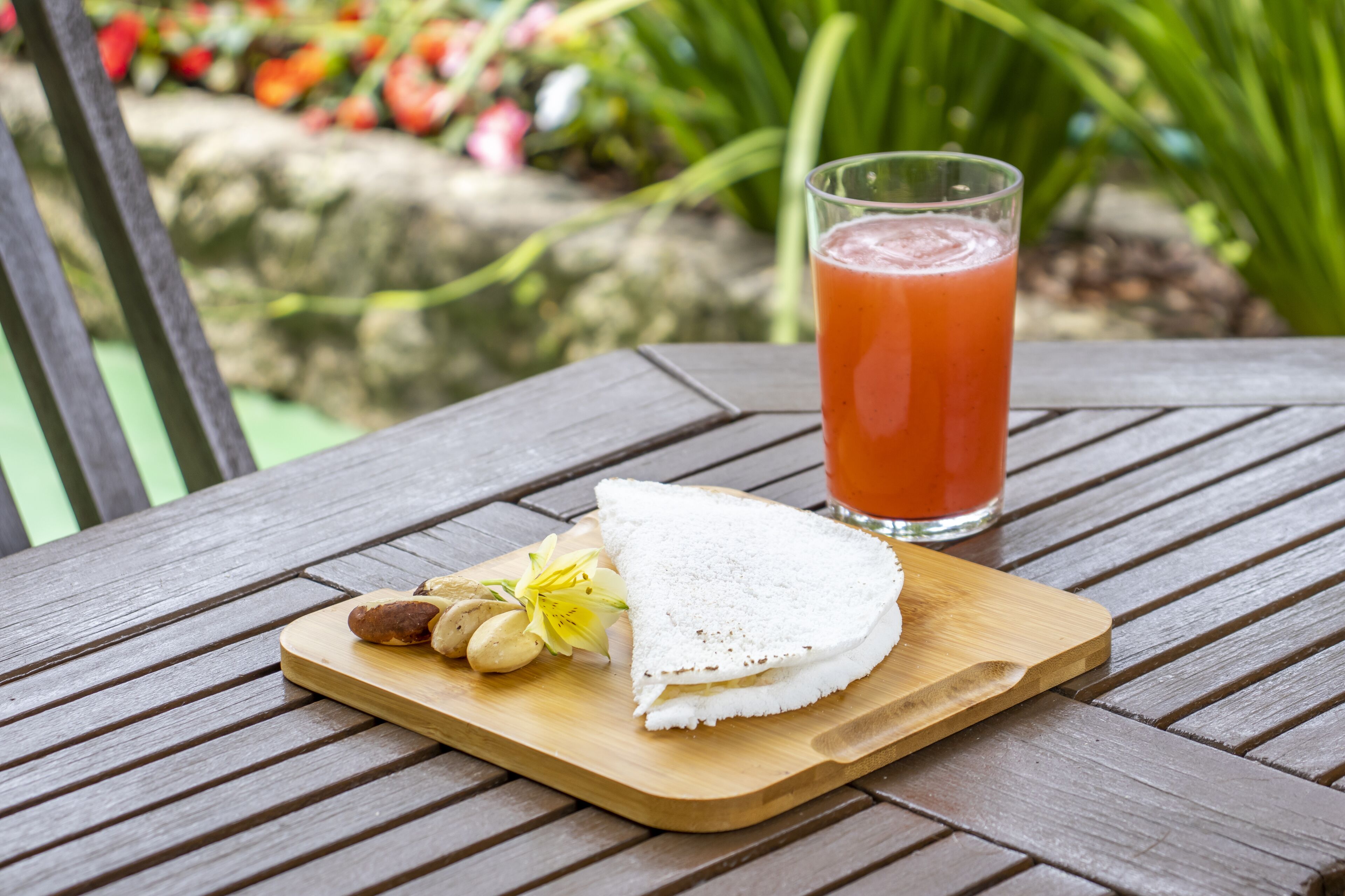 Een houten tafel met een glas jus d'orange, een belegd broodje en wat noten.