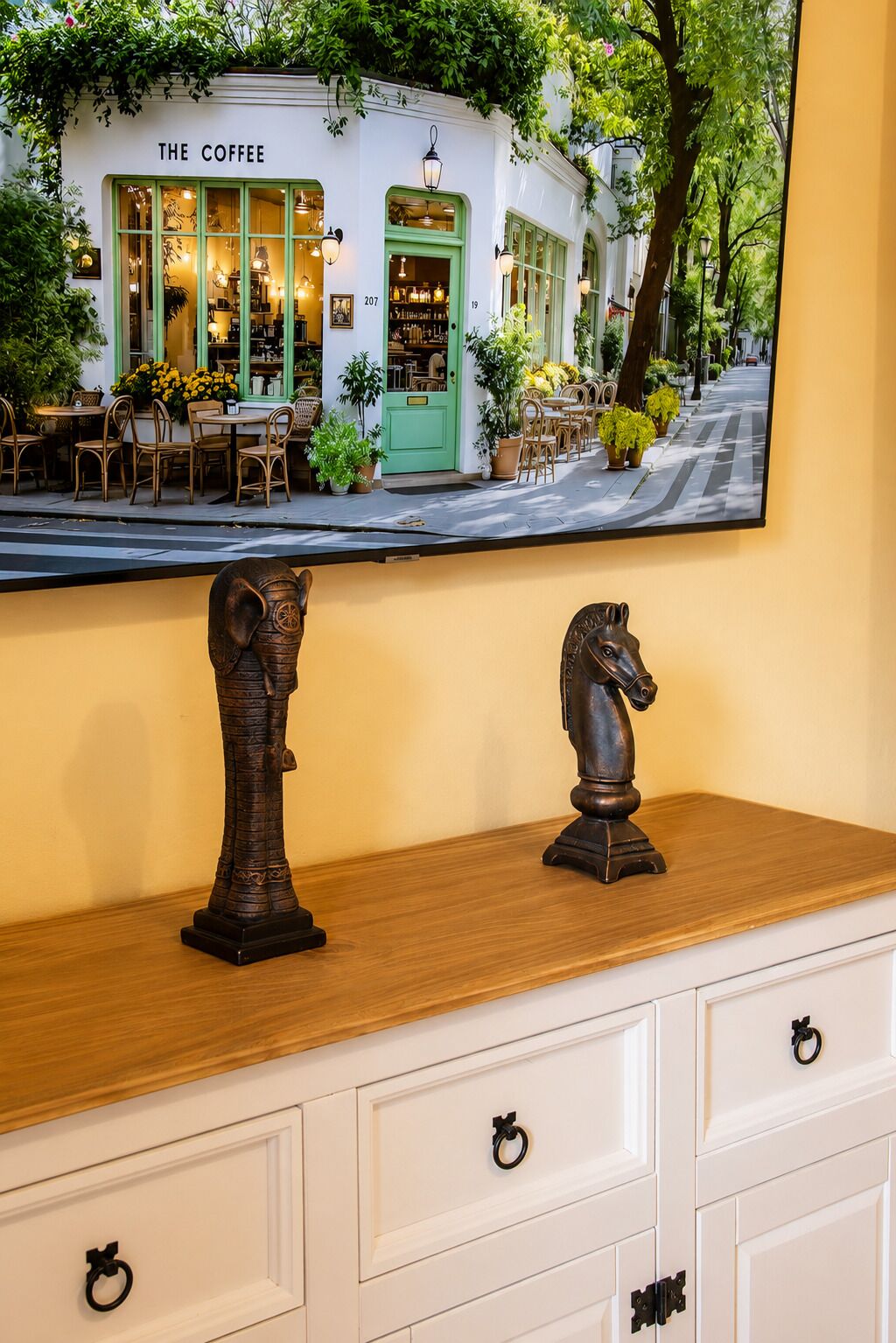A wooden dresser with two horse sculptures and a mirror reflecting a cafe named 'The Coffee' with outdoor seating.