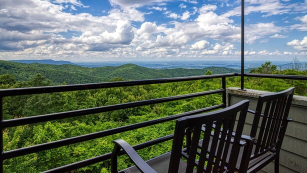 A balcony with a view of a lush green landscape and distant mountains under a partly cloudy sky.