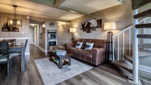 A modern living room with a brown leather sofa, a dining table, and a staircase.