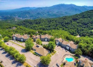 An aerial view of a residential area with multiple houses, a swimming pool, and a mountainous backdrop.