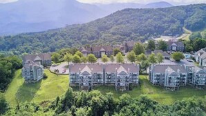 A residential area with multiple two-story houses, surrounded by lush greenery and mountains in the background.