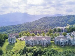 A residential area with multiple two-story houses, surrounded by lush greenery and mountains in the background.
