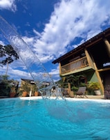 Piscina com água azul cristalina, rodeada por plantas em vasos e um deck de madeira.