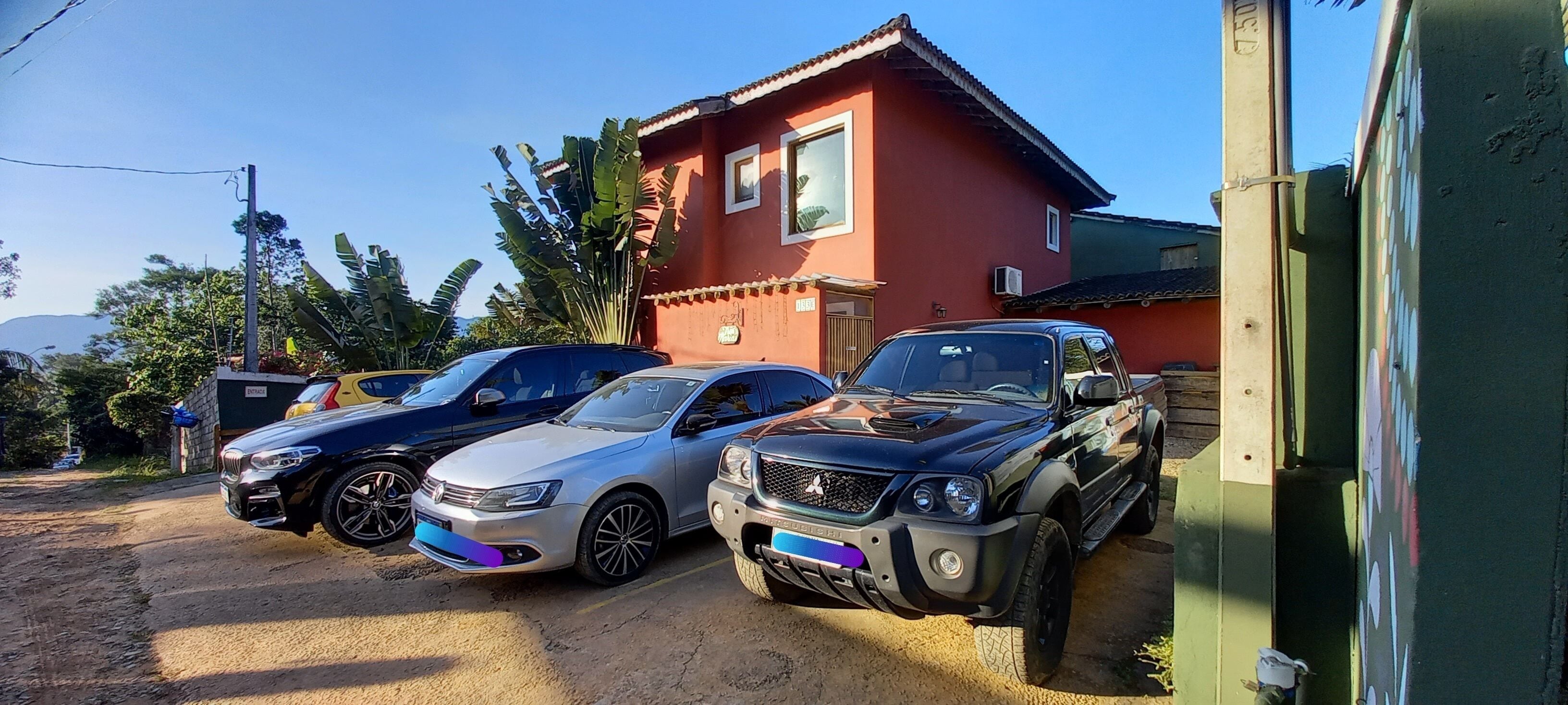 Three cars parked in front of a red house with a large window and a door.