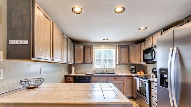 A modern kitchen with wooden cabinets, a stainless steel refrigerator, and a tiled island. - ATV Trail Access! Secluded Mountain Retreat (Duff)