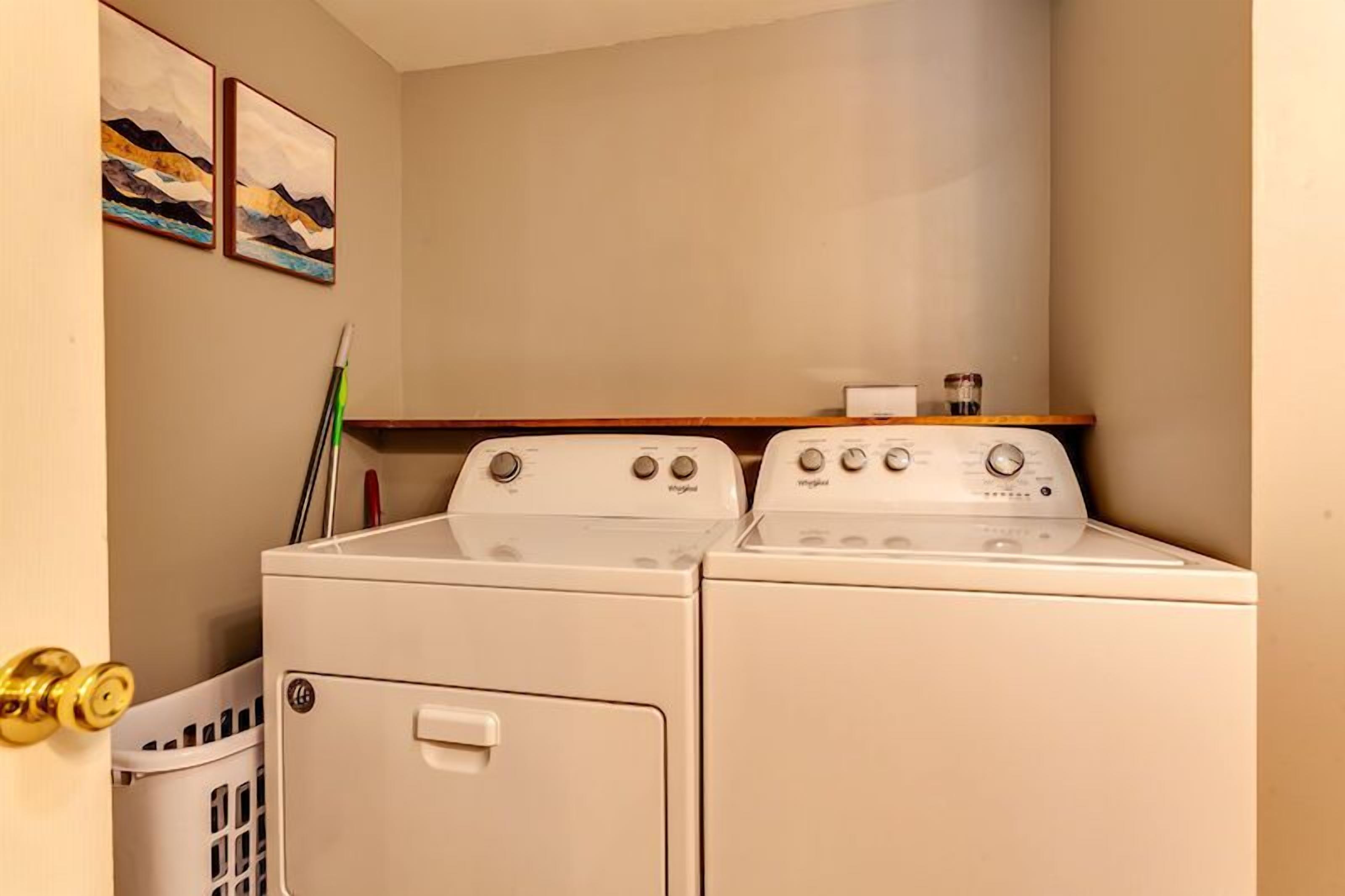 Una lavanderia con due lavatrici e asciugatrici bianche Whirlpool, uno scaffale di legno con un piccolo oggetto e una porta con maniglia dorata.