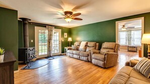A living room with a dark green wall, a ceiling fan, a fireplace, a sofa, a recliner, and a lamp. - ATV Trail Access! Secluded Mountain Retreat (Duff)