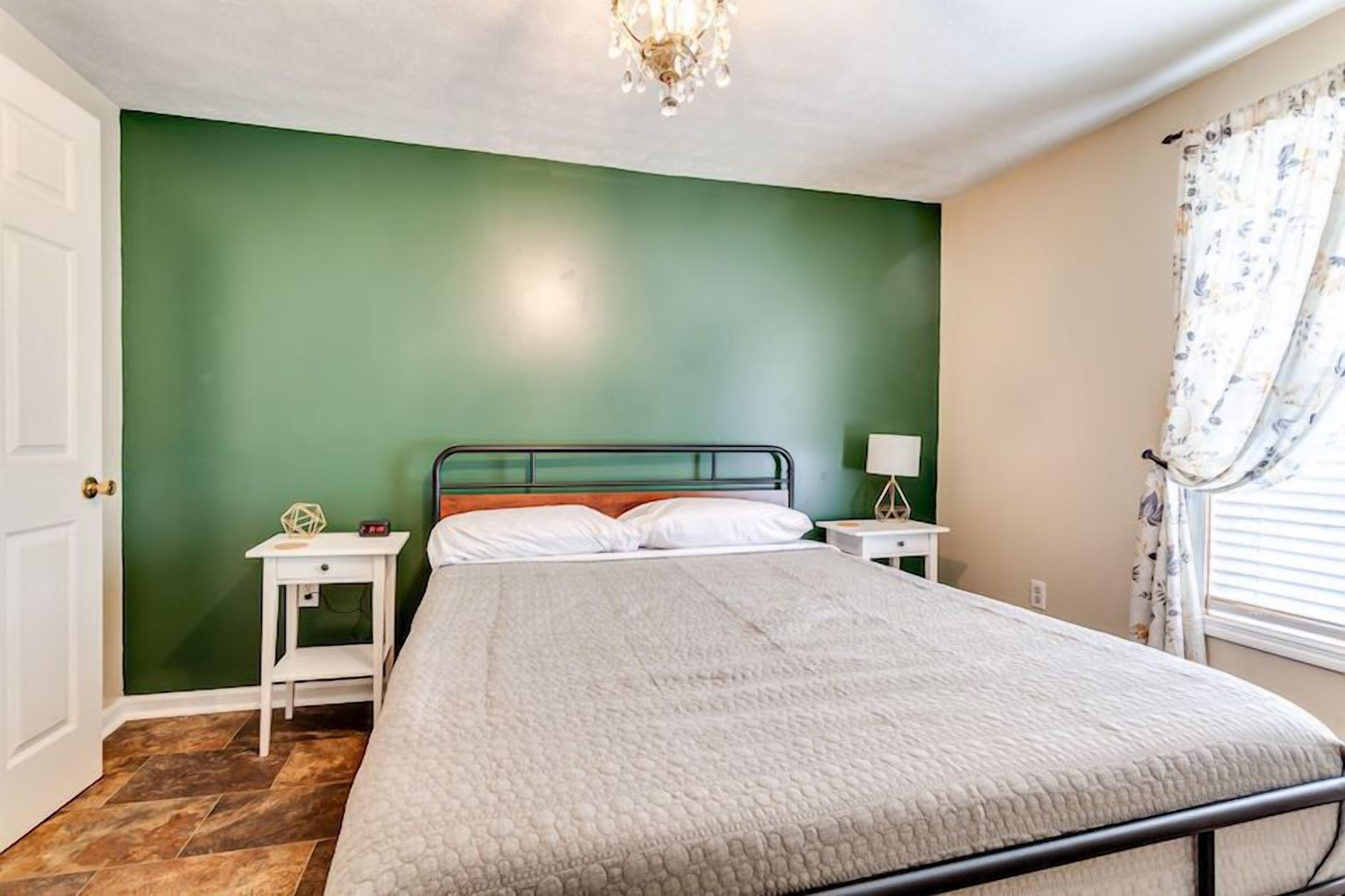 A bedroom with a bed, a nightstand, a lamp, and a window with curtains.