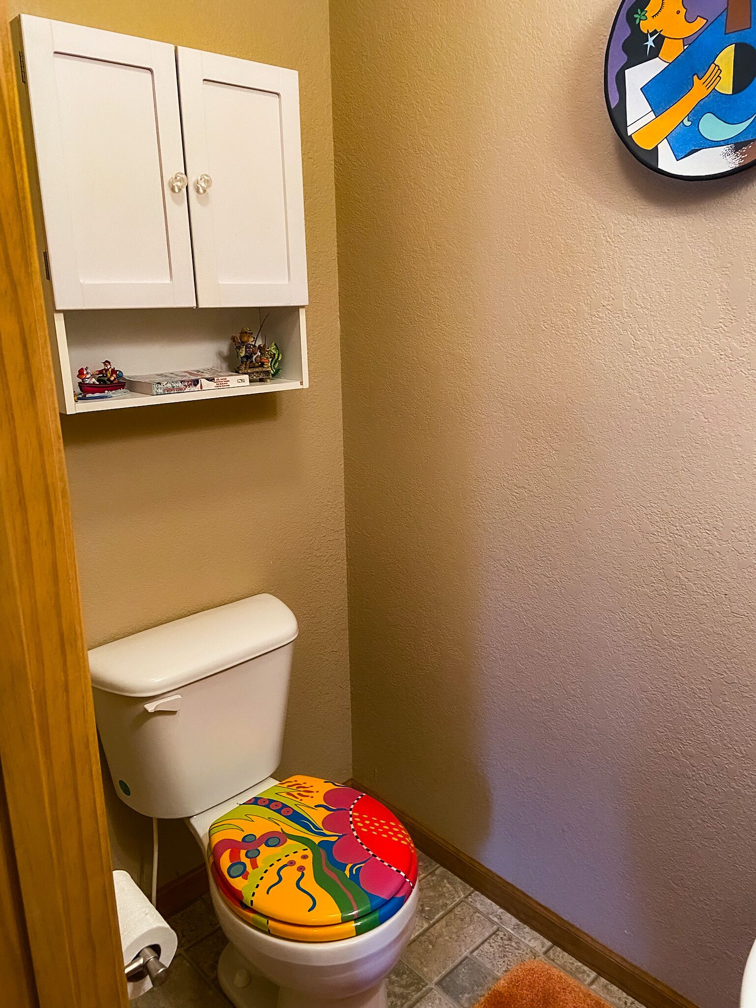 Een badkamer met toilet, een kast erboven en een plank met decoratieve objecten.