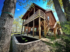 Une cabane en bois dotée d’un balcon, entourée d’arbres et d’un petit jardin.