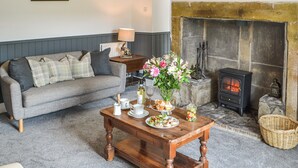 Una sala de estar acogedora con un sofá gris, una mesa de centro de madera con un centro de mesa floral, una chimenea y una pared de piedra.