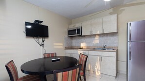 A compact kitchen with a dining area, including a TV mounted on the wall, a microwave, a refrigerator, and a tiled backsplash. - Red Sunset Beach Club (Cabo Rojo)