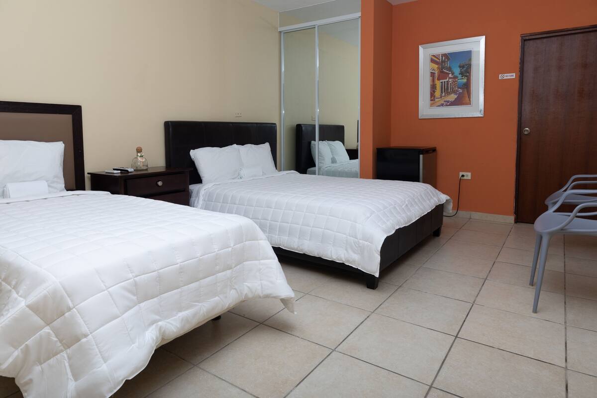 A hotel room with two beds, a wardrobe, a chair, and a painting on the wall.