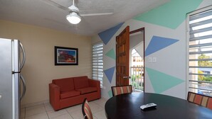 A dining area with a round table, chairs, a red sofa, and a ceiling fan. - Red Sunset Beach Club (Cabo Rojo)