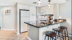 A modern kitchen with a central island, bar stools, stainless steel appliances, and pendant lighting. - Beachfront “Our Happy Place” Ground Level 2/2 sleeps 8 (Gulf Shores)