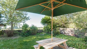 Ein Holztisch für ein Picknick mit einem grünen Sonnenschirm, umgeben von einer Steinmauer und Pflanzen.