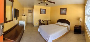 A hotel room with a bed, a desk, a chair, a TV, a ceiling fan, and artwork on the walls.
