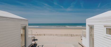 Vista da praia com duas cabanas de praia brancas e um caminho de areia que leva ao oceano.
