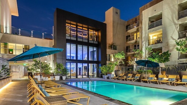 A modern hotel with a swimming pool, lounge chairs, and a large building with balconies.