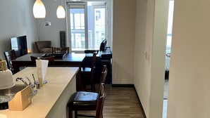 A modern kitchen with a central island, wooden flooring, pendant lighting, and a view of the city through large windows.