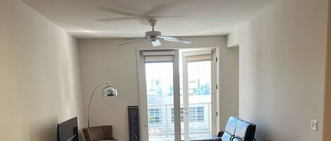 A modern living room with a dining area, a ceiling fan, a TV, and a view through the door.