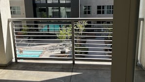 A balcony with a view of a modern building, a pool, and potted plants.