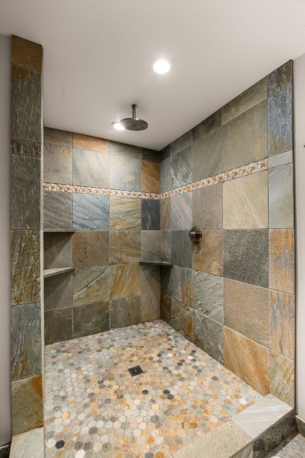 A shower area with stone tiles and a mosaic floor.