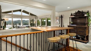 A spacious room with a wooden bar, large windows, a staircase, and a dark wooden cabinet.