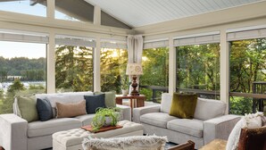 A spacious room with a large window, a sofa, a chair, and a lamp.