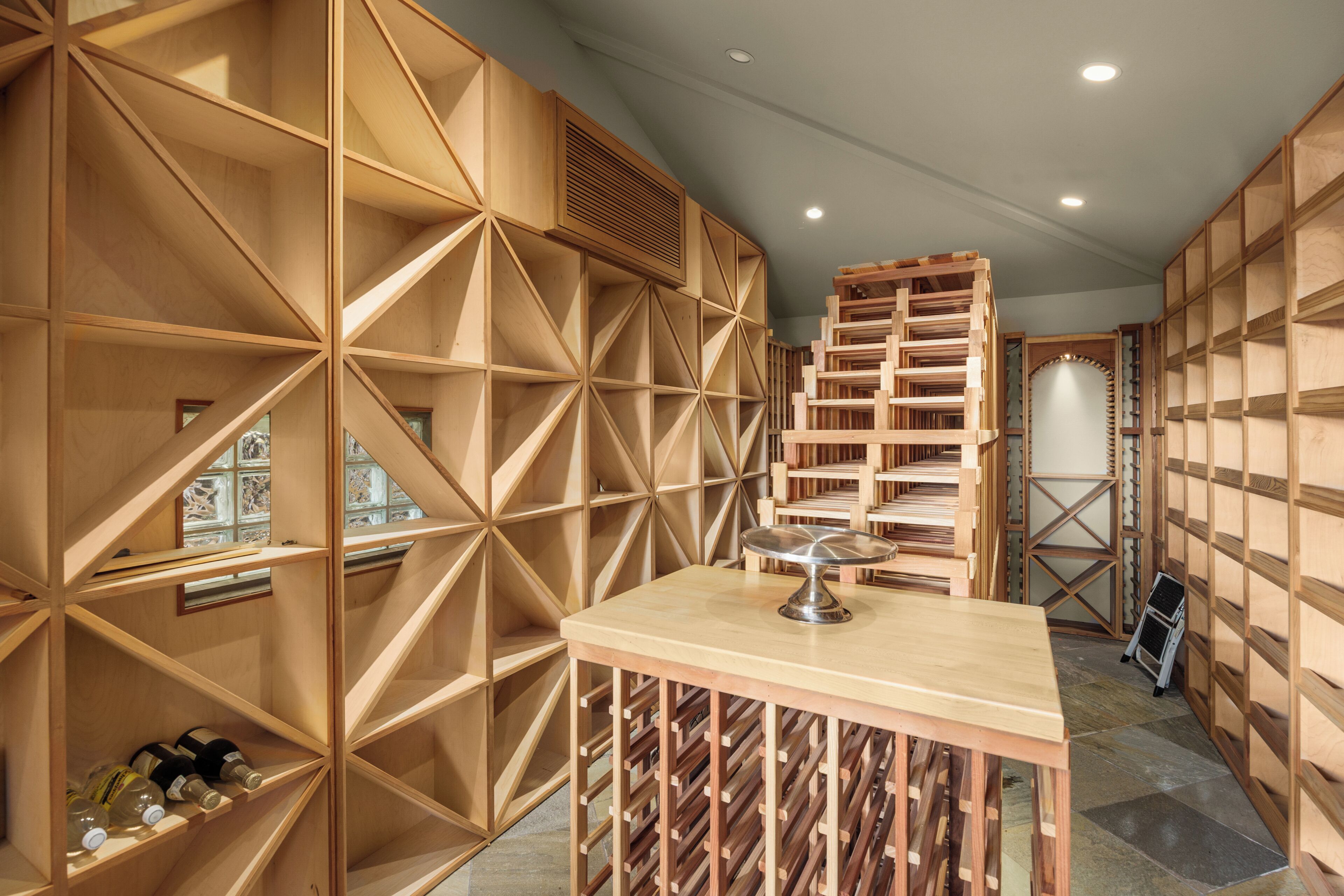 A wine cellar with wooden shelves and racks, a small table with a metal object, and a ladder.
