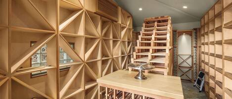 A wine cellar with wooden shelves and racks, a small table with a metal object, and a ladder.