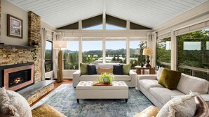 A spacious living room with a fireplace, large windows, and a view of the outdoors.