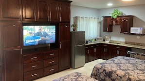 Un espace de vie compact comprenant une kitchenette, un téléviseur et un ventilateur de plafond.