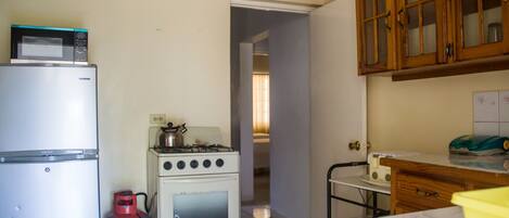 A compact kitchen with a refrigerator, stove, and gas cylinder.