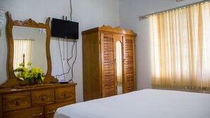 Una habitación con un armario de madera, una cama, un tocador con espejo y un televisor montado en la pared.