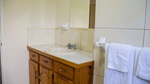 Un baño con tocador de madera, un lavamanos, un espejo y una toalla colgada en la pared.