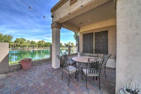 A patio with a round table and chairs, a view of a body of water, and a pergola with string lights.