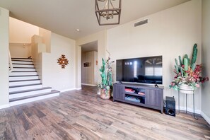 A modern living room with a staircase, a flat-screen TV, a dark wooden entertainment unit, and two potted plants.