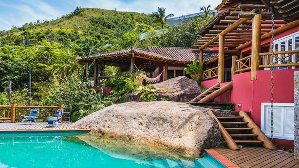 A pool with wooden steps and a red building in the background. - Mansão Sobreomar - Ilhabela (Ilhabela)