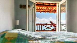 A bedroom with a bed, a window, and a view of the sky and mountains. - Mansão Sobreomar - Ilhabela (Ilhabela)