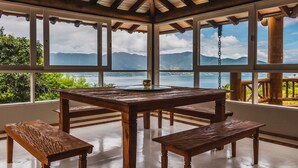 A wooden gazebo with a glass table and benches, overlooking a mountainous landscape and a body of water. - Mansão Sobreomar - Ilhabela (Ilhabela)
