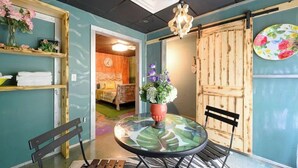A room with a round glass table, two chairs, a wooden bench, a potted plant, a wooden door, and a wall-mounted shelf with flowers. - HOCHATOWN Charming Hotel Garden suite. (Broken Bow)