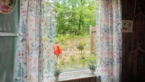 A window with floral curtains, a view of a garden with a wooden fence, and a welcome sign. - HOCHATOWN Charming Hotel Garden suite. (Broken Bow)