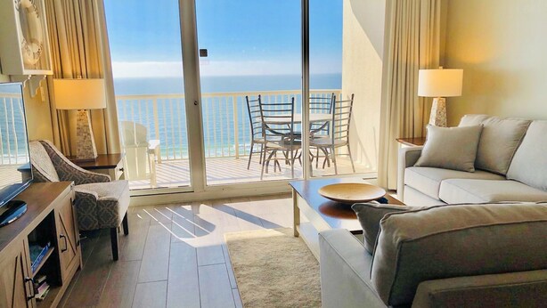 A hotel room with a balcony, a sofa, a TV stand, and a dining area with chairs and a table.