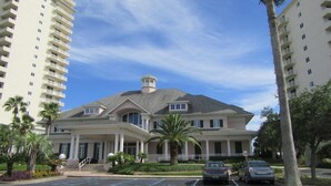 A large, two-story building with a central entrance and a covered porch. There are palm trees and a parking lot in front.