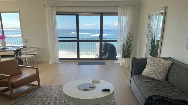 A modern living room with a large balcony overlooking the sea, a round coffee table, and a grey sofa. - Beachfront Penthouse at The Entrance - Beach Pool right infront (The Entrance)