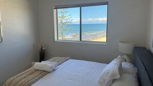 A bedroom with a large window, a bed with white linens, a bedside lamp, and a view of the beach and ocean. - Beachfront Penthouse at The Entrance - Beach Pool right infront (The Entrance)